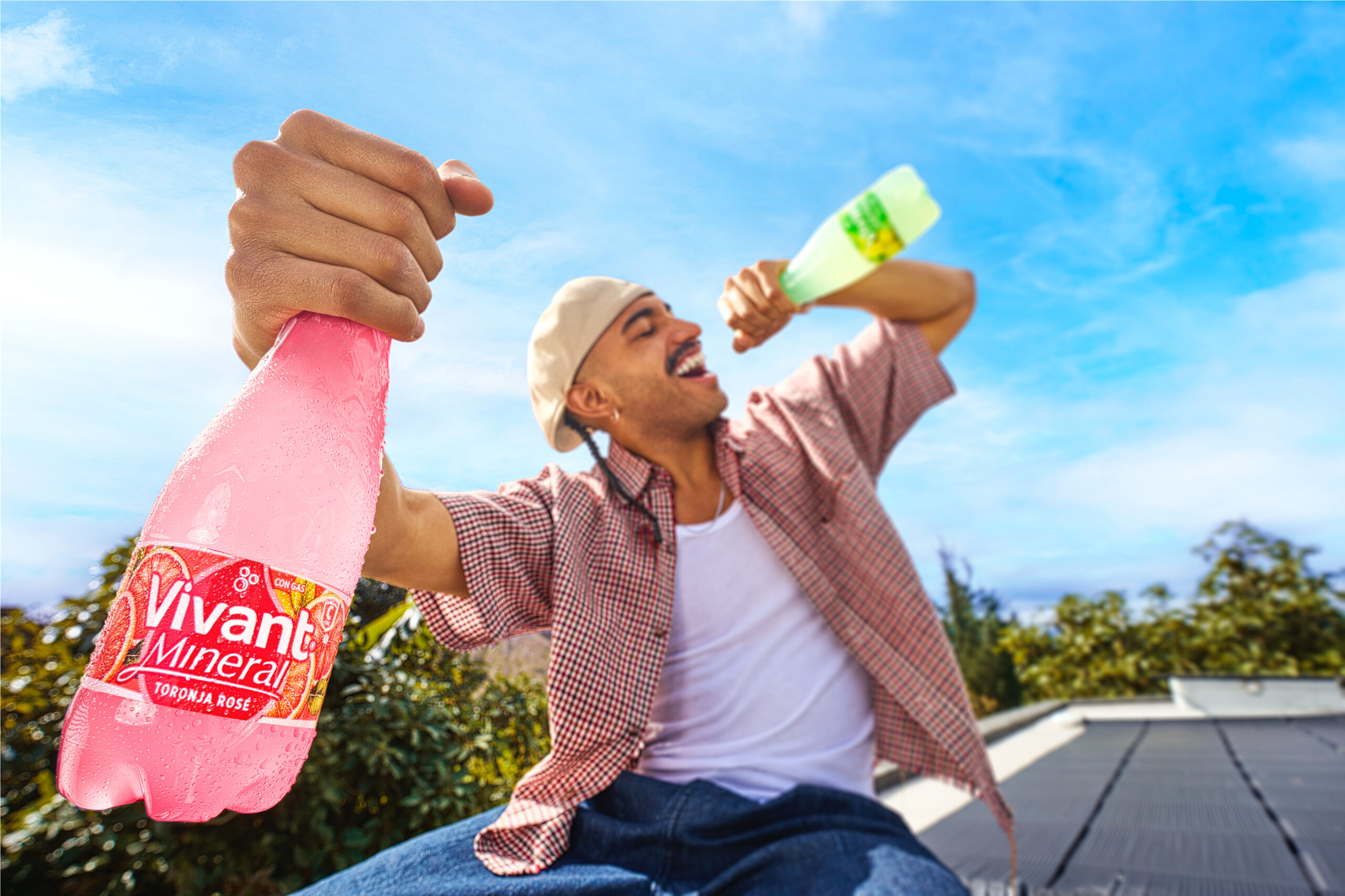 Hombre en una azotea sosteniendo en alto una botella de Vivant Mineral, cielo despejado de fondo.
